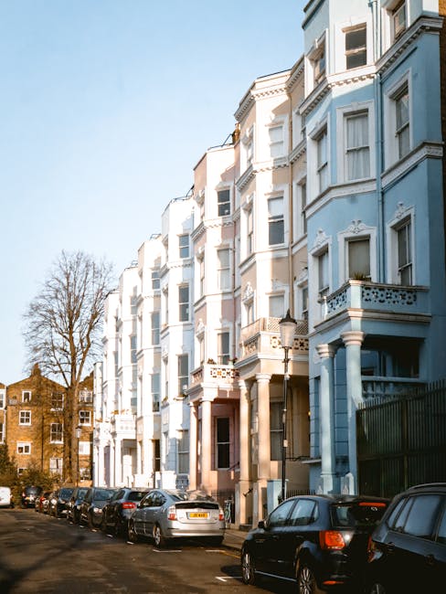 A row of four-story Victorian-style terraced houses on a street in Notting Hill, London, with each building painted in a different vibrant colour—cream, dark blue, bright green, and pink. The buildi